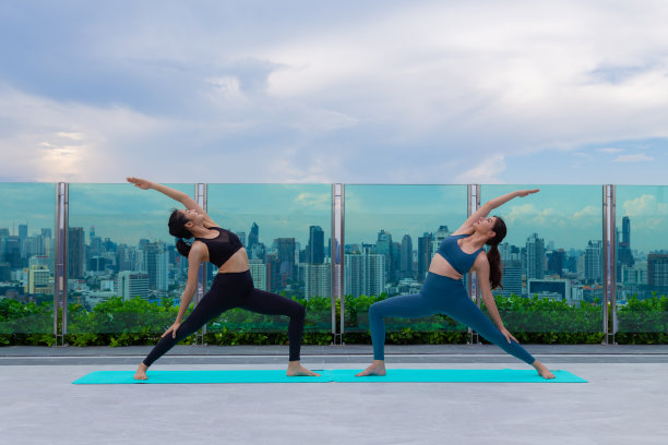 年轻的亚洲女性做劈叉运动，练习瑜伽或普拉提。在高楼的屋顶上，女人自然美丽和健康，眺望着美丽的城市景色。图片下载
