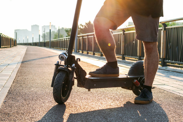 一个男人的脚在运动鞋停止站在电动摩托车上骑在街上或公园工作后的户外。有选择地关注脚。图片下载