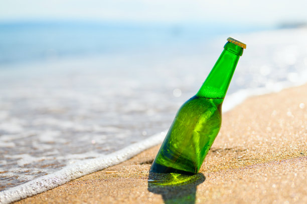 在沙滩上，以大海为背景，在沙滩上的沙子里喝一瓶啤酒。娱乐的概念。图片下载