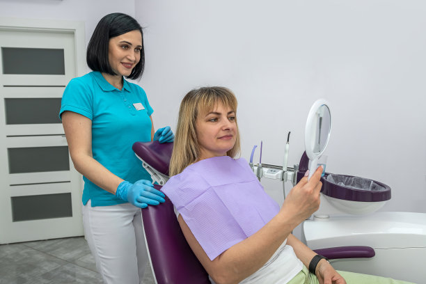 年轻漂亮的病人看着靠近牙医的镜子，评价他的工作。图片下载