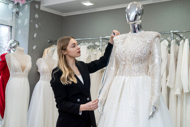 迷人的女售货员在时尚的黑色西装测量婚纱用卷尺图片下载