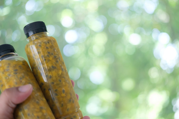 在模糊的自然背景下，手拿着一瓶百香果的塑料瓶图片下载