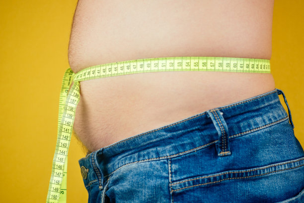 一个胖子肚子上夹着一根卷尺。不健康营养的概念图片下载