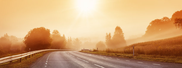 在晨雾中，黑色的柏油路有分界线和安全栅栏。图片下载