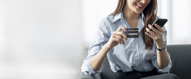 年轻美丽的亚洲女子使用信用卡通过智能手机在家里网上购物。素材图片