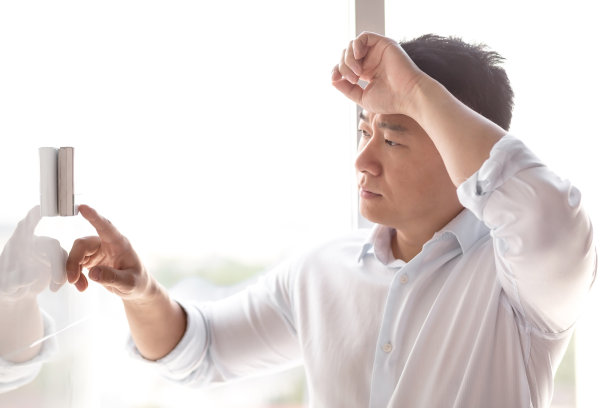 一个亚洲人打开挂在墙上的空调控制按钮。站着,很热图片下载