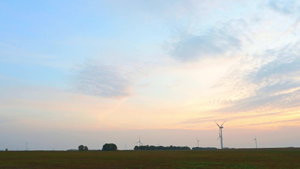 风力涡轮机在海上风力发电场在绿色的田野在太阳低日出特写。图片下载