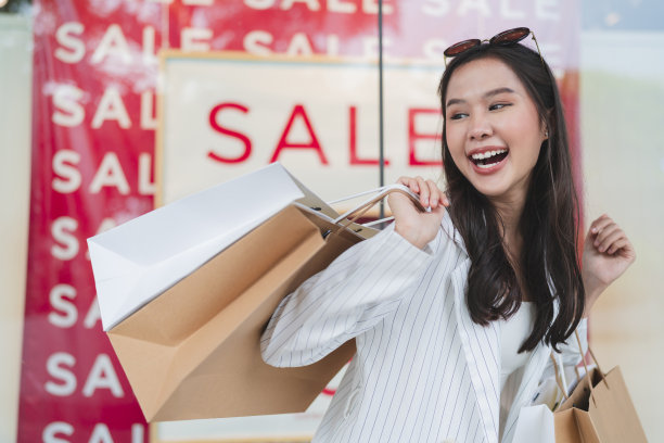 快乐微笑的亚洲妇女女孩拿着一堆购物袋，女性购物后回家，她买了许多衣服在一个合理的价格，而在商店橱窗展示商店打折销售图片下载