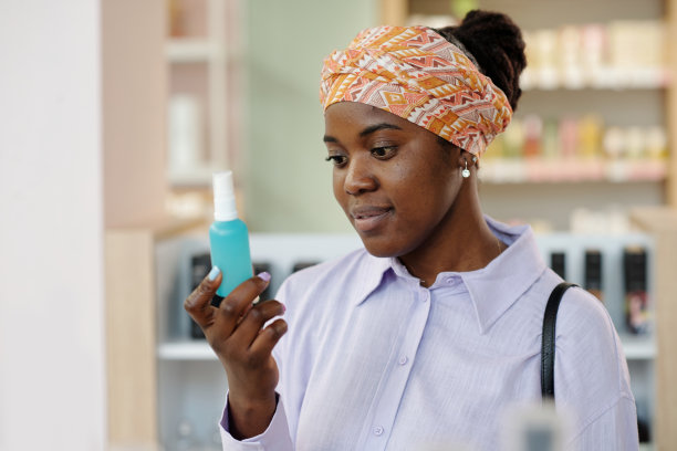 快乐的年轻黑人妇女看着装着蓝色液体美容产品的瓶子图片下载