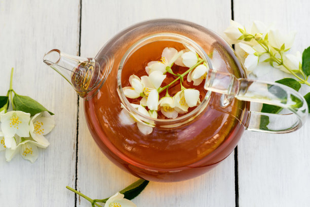 茉莉茶和花在玻璃茶壶上的木制白色背景，接近。茉莉花茶茶壶图片下载