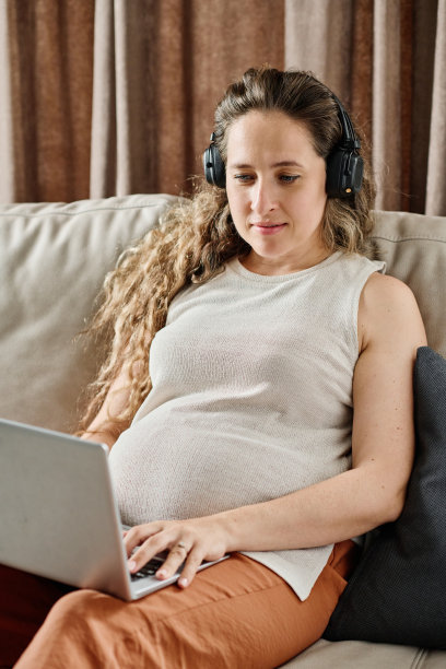 年轻孕妇戴着耳机，悠闲地看网络视频图片下载