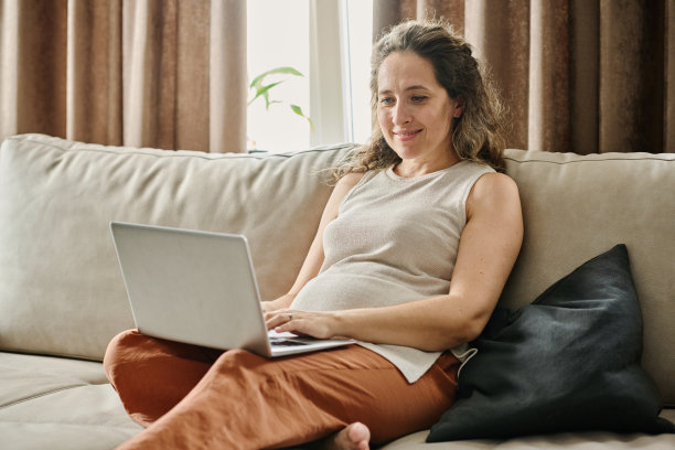 快乐的年轻怀孕女商人或女性自由职业者在笔记本电脑上打字图片下载
