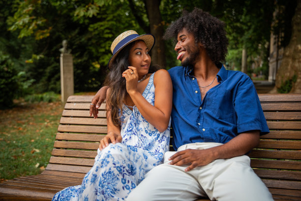 一对情侣坐在长椅上共度片刻，女友被男友的脸吓到了。图片下载