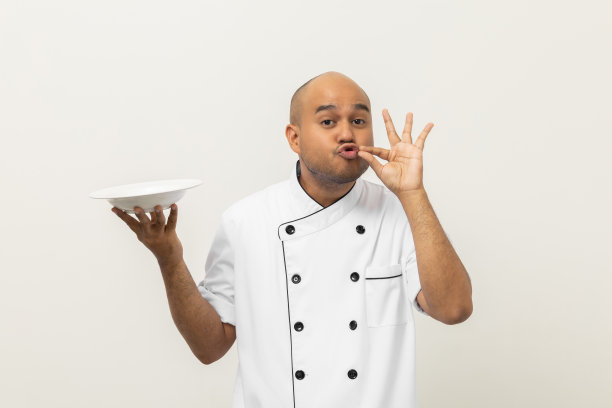 微笑年轻英俊的亚洲男子厨师在制服拿着空盘子美味的菜菜单好味道上孤立。烹饪印度人职业厨师或面包师，厨房、餐厅和酒店的人。图片下载