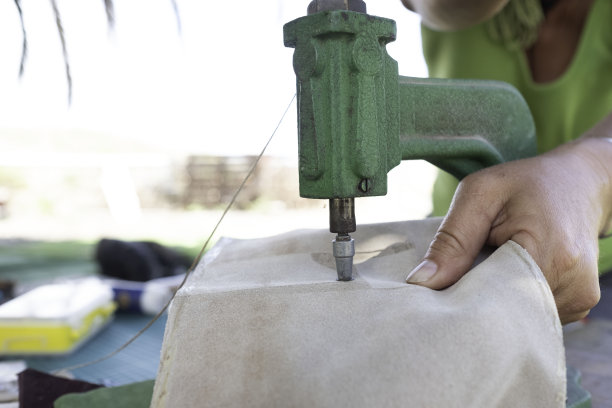在她的小作坊里工作的工匠。用铆接压力机加工皮革制作钱包的工匠。图片下载
