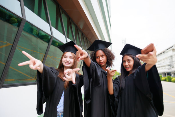学生穿着长袍，用智能手机拍照，即将毕业。祝毕业成功并庆祝。祝贺图片下载