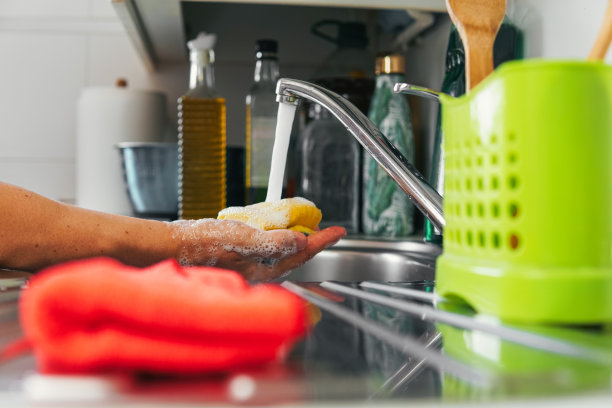 手握黄色洗涤垫与手掌，水从水龙头落下。制作肥皂和泡沫的洗碗器具的侧面照片。清洁的概念图片下载