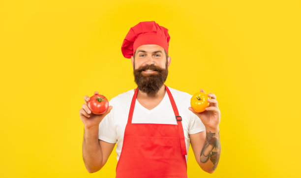 快乐的男人穿着围裙和无边帽，拿着红黄相间的西红柿做黄色的底色，做饭图片下载