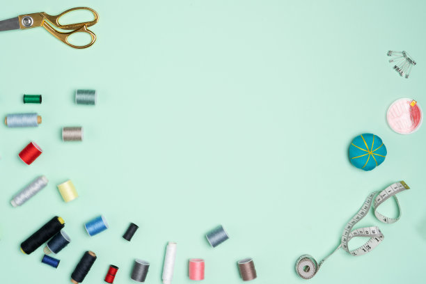 绿色的背景上排列着许多五颜六色的线轴。缝纫配件、剪刀、卷尺、钮扣。图片下载