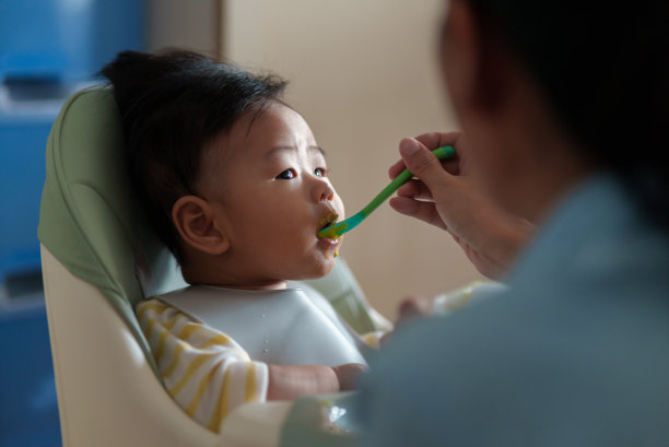 坐在高椅子上的亚洲小男孩正在被妈妈喂食。图片下载