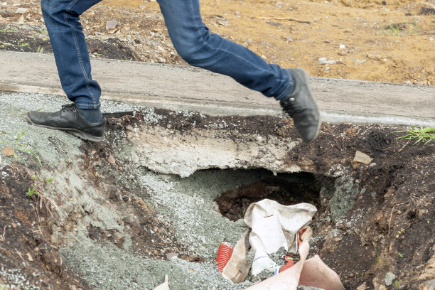 一名男子的双脚跃过沥青人行道旁的一个坑。图片下载