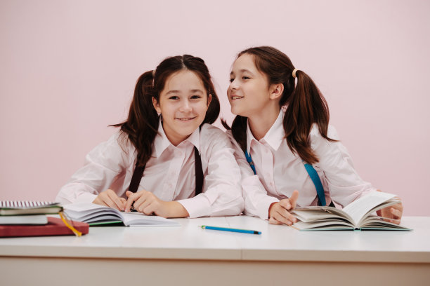 八卦好奇的双胞胎女学生坐在课桌后面拿着课本图片下载