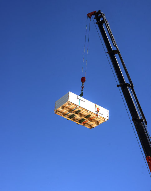 一台起重机将一堆太阳能电池板吊到屋顶进行安装。可再生能源装置概念图片下载