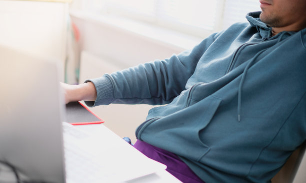 一个穿着绿松石毛衣的男人在明亮的办公室里对着电脑工作。工作说明。图片下载