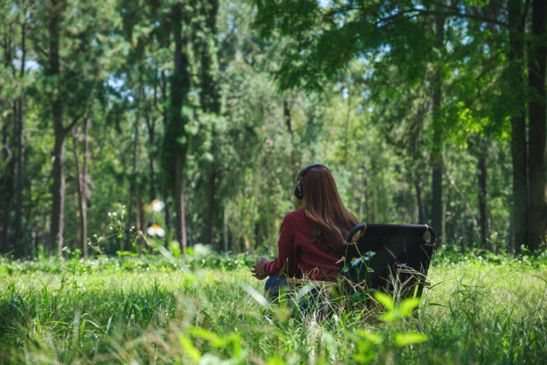 一名年轻女子坐在公园的露营椅上，用耳机听音乐图片下载