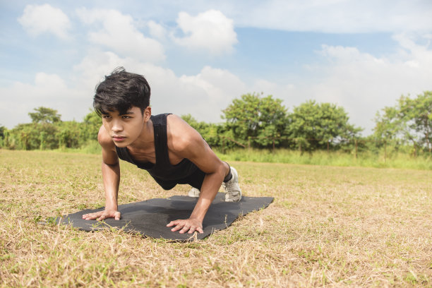 一个健康的亚洲男人在户外的一块黑色垫子上做着常规的俯卧撑。胸部或全身锻炼。图片下载