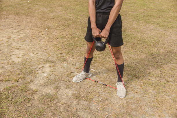 一个适合的亚洲球迷表演壶铃摆动与阻力带的先进版本。在开阔的草地上锻炼上身和肩部。图片下载