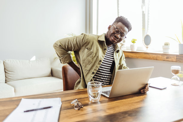 一个年轻的商人在他的办公桌上工作时经历背痛。图片下载