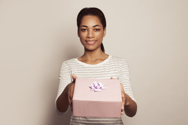 年轻开朗的微笑的女人显示粉红色的礼物在白色的背景图片下载
