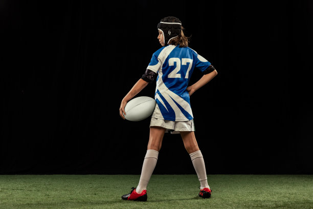 动态肖像学龄男孩，少年男子橄榄球运动员练习橄榄球孤立在黑暗的背景与草地地板。图片下载