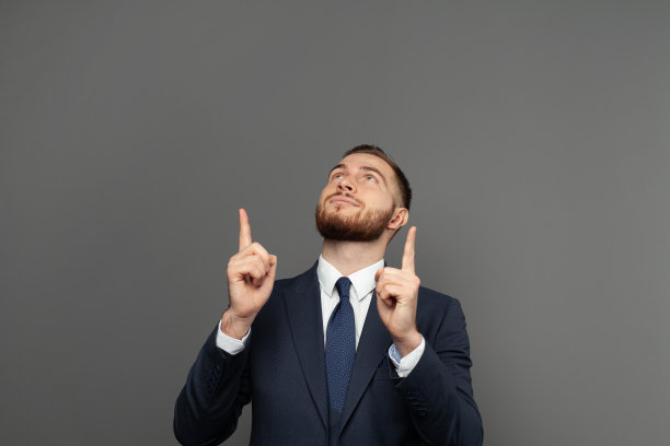 一个幸福的商人的肖像在灰色的背景上手指向上图片下载