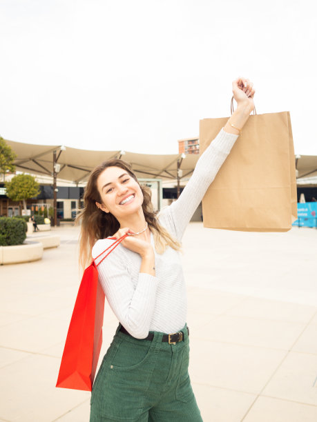 微笑的年轻女子在商场里提着购物袋。购物的概念图片下载