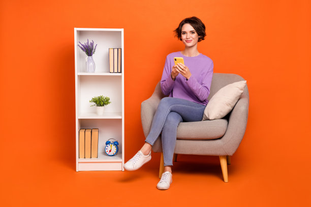 完整的照片可爱甜美的女士穿紫色运动衫坐在椅子上聊天小工具孤立的橙色背景图片下载