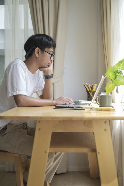 侧面的年轻自由职业者使用电脑笔记本电脑，而坐在舒适的家庭办公室。图片下载