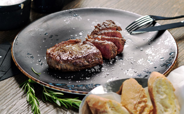 特写镜头切成中等熟牛排与餐具盘子和碗与新鲜烘焙的面包图片下载