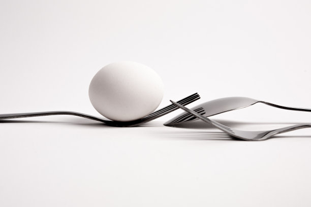 鸡蛋放在金属叉子上，勺子孤立在白色背景特写。鸡蛋放在两个叉子、勺子上。从饮食到烘焙，鸡蛋有很多用途。图片下载