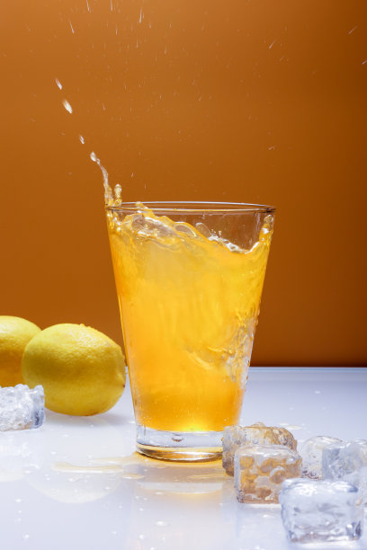 橙色背景上的玻璃溅水和冰块图片下载