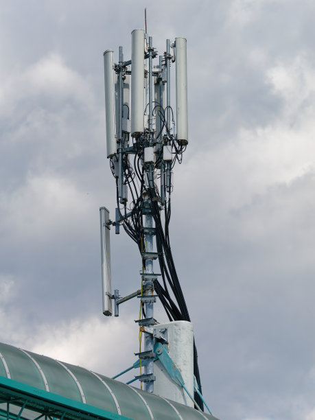 在多云的天空下，手机基站或手机信号塔在建筑物顶上的垂直照片图片下载