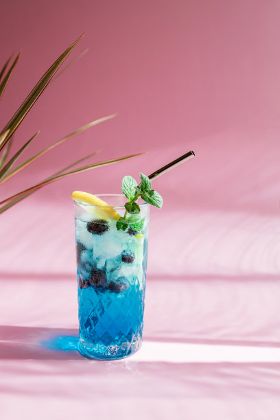 清爽的夏天五颜六色的蓝色饮料在粉红色的背景与潮流的阴影。库拉索甜酒配新鲜蓝莓和柠檬片图片下载