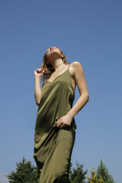 户外形象的年轻女子在绿色丝绸长裙对清晰的蓝天图片下载