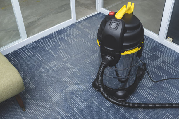 一个镀铬直立式吸尘器放在办公室角落的地毯地板上。图片下载