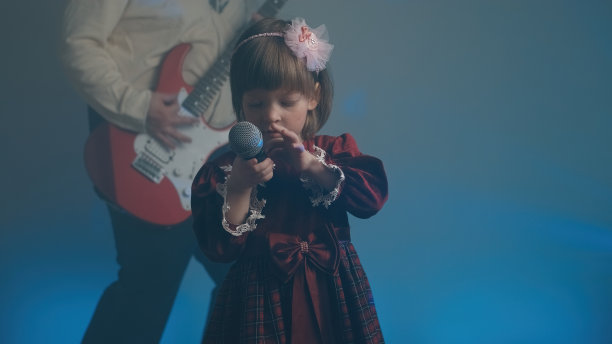 穿着复古礼服的小女孩在舞台上唱歌，她的父亲在弹奏电吉他图片下载
