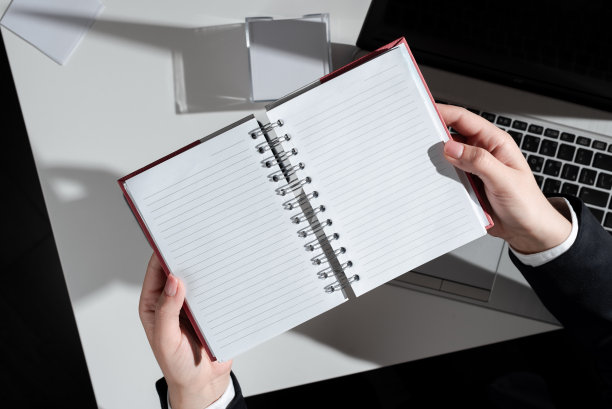 商业女性拿着笔记本电脑与新的想法超过书桌与笔记和笔记本电脑。穿着西装的女人有一个记事本，上面有重要的信息，有备忘录和电脑。图片下载