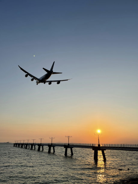 在充满活力的日落天空下，一架飞机在海上飞行的沿海视图，香港图片下载