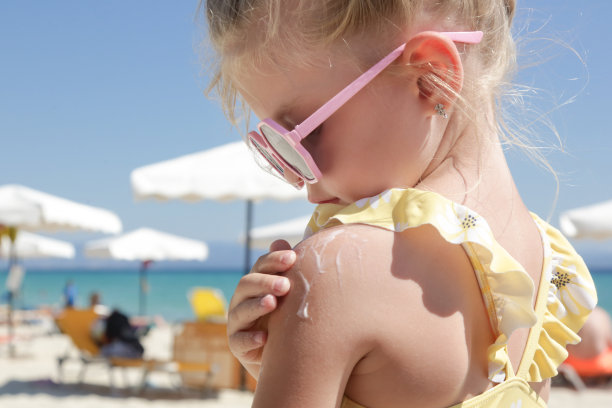 可爱的4岁小女孩在沙滩上涂防晒霜。防晒乳液，暑假期间保护孩子免受阳光伤害。旅行期间的儿童皮肤护理。图片下载