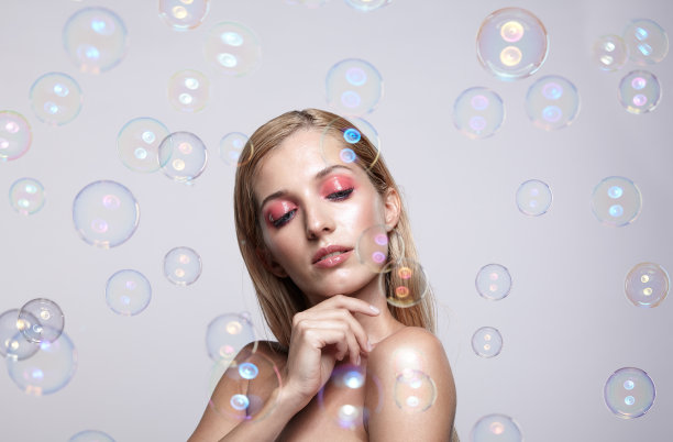 漂亮的年轻金发女人，灰色的背景上有肥皂泡图片下载